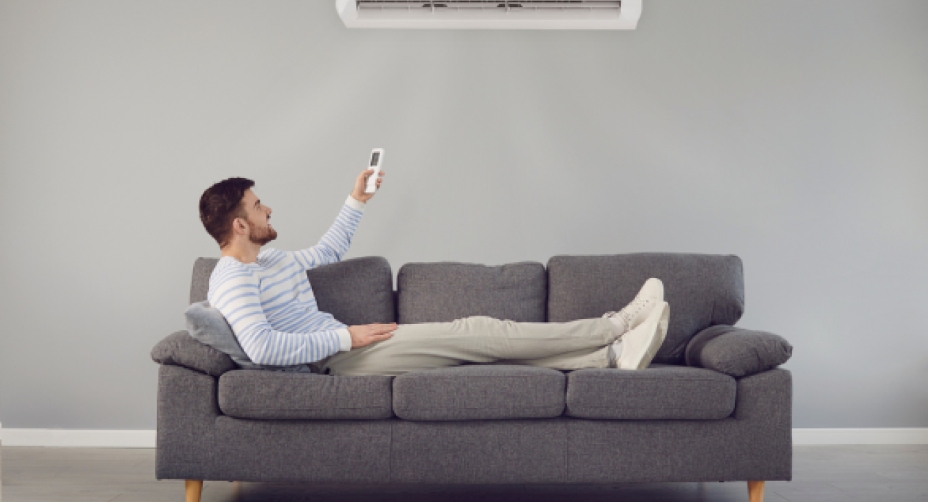 Man reclining on grey sofa turning on his Home Air Conditioning Installation - Pure Electrical Solutions in Twickenham